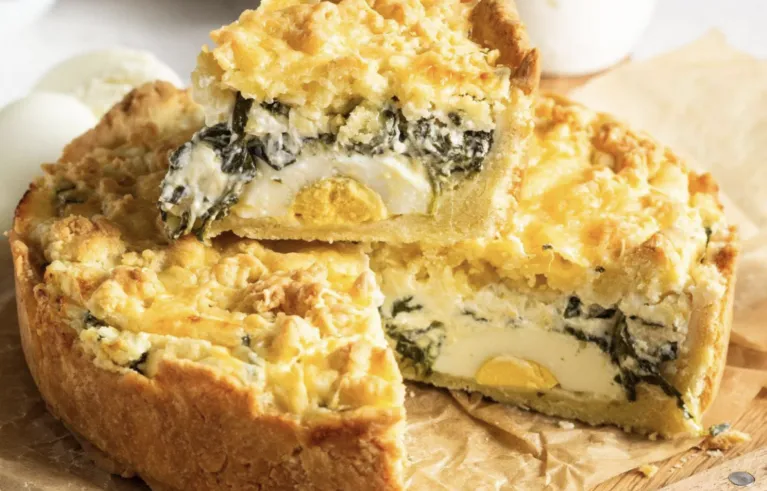 Torta Pasqualina, on a wooden board, cut open to show the spinach, eggs and ricotta.